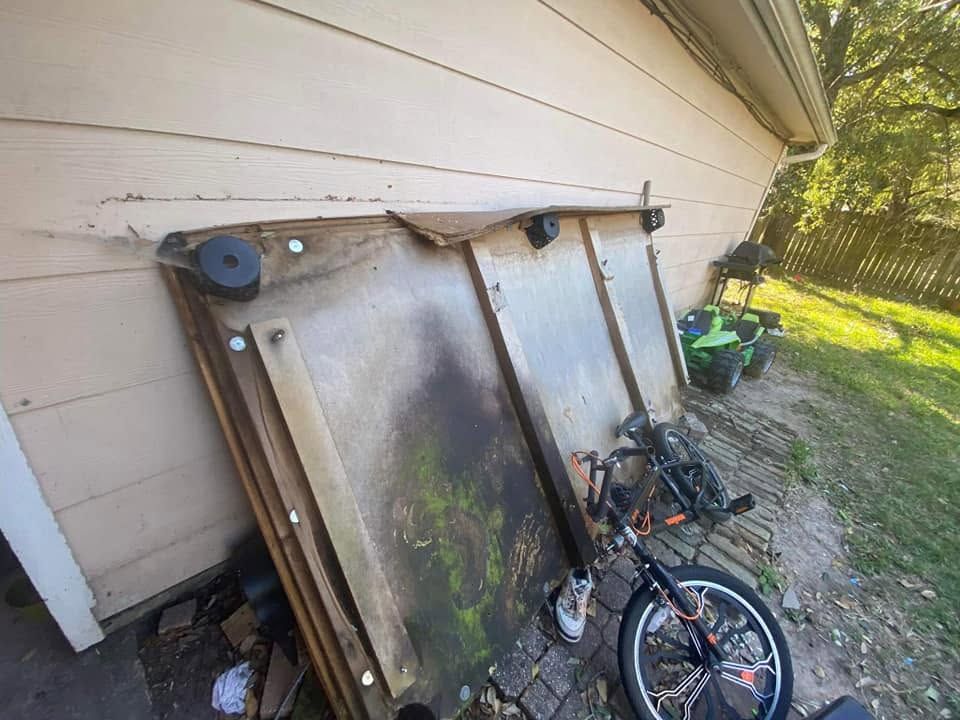 Old metal doors and a bicycle leaning against a house exterior in a yard