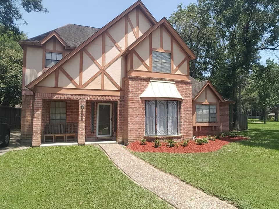 Tudor-style brick house with steep gables, a curved walkway, and a green lawn under trees.