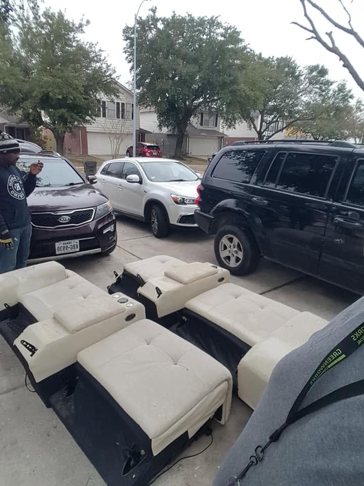 Broken white lounge seats stacked on a sidewalk beside parked cars and a person on a residential street