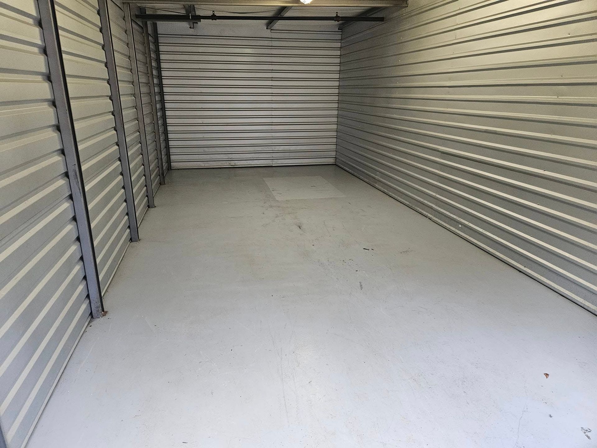 Empty indoor storage unit with white walls, gray metal doors, and concrete floor