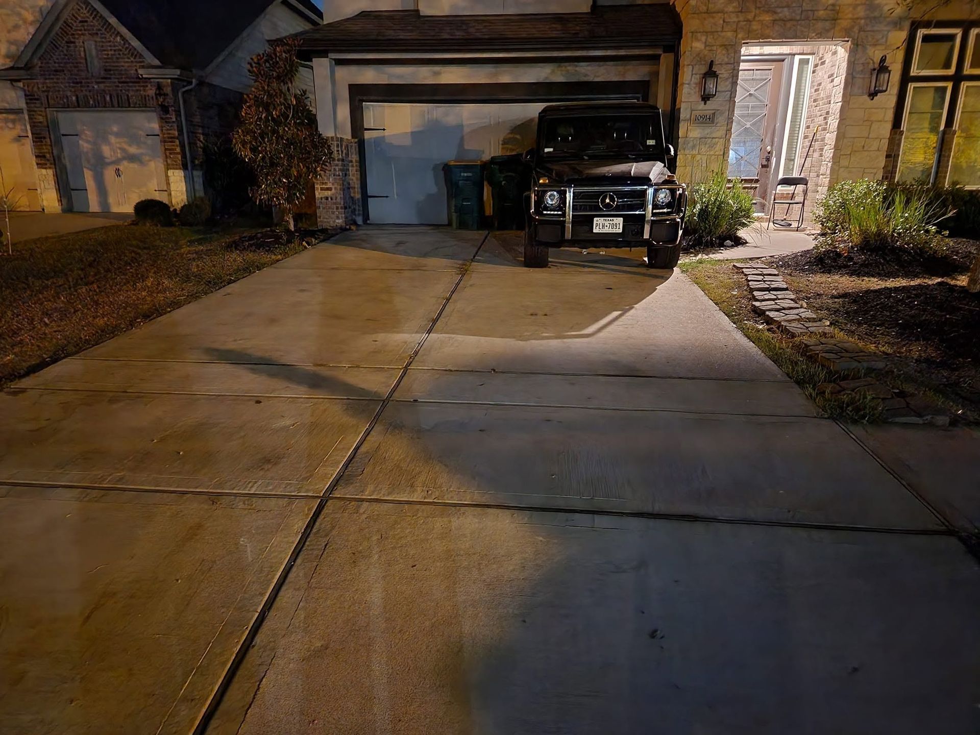 Two-car garage at night with a black SUV parked in the driveway and porch lights on.