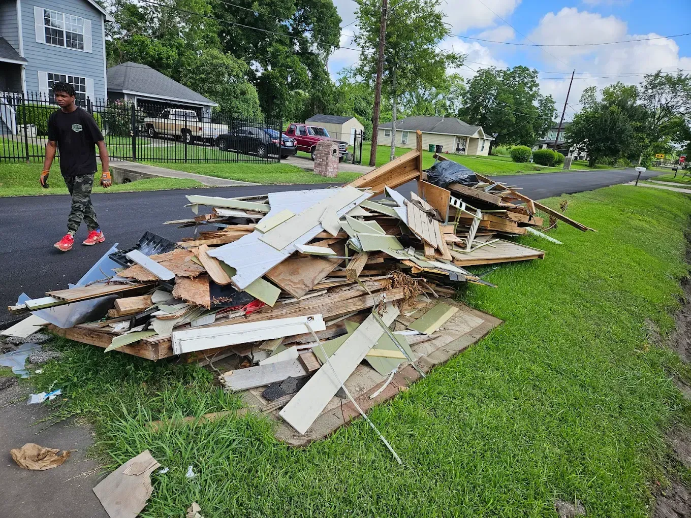 Pile of demolition debris along a grassy roadside near houses and a person standing nearby