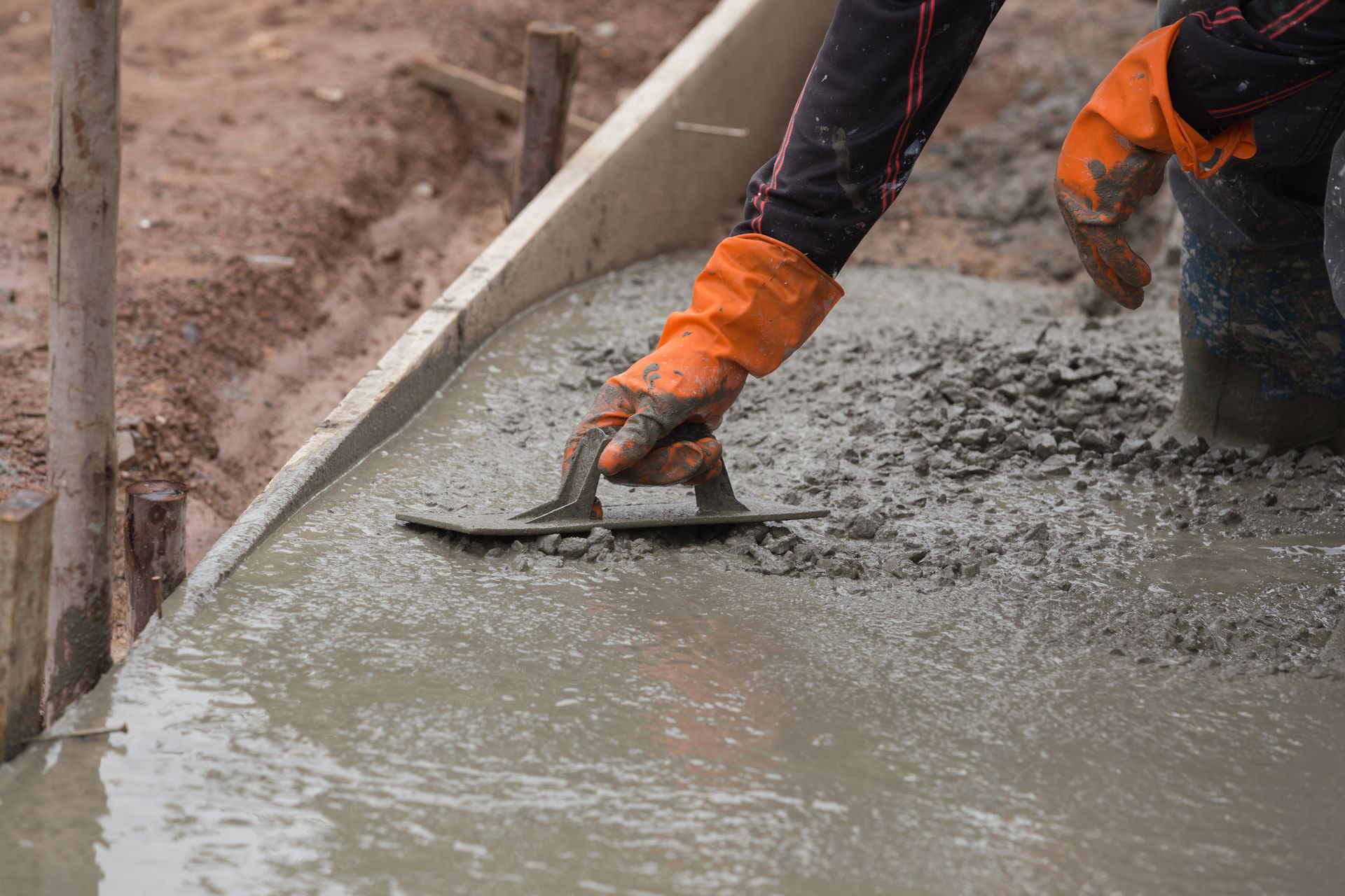 A gloved hand uses a trowel to level concrete poured on the ground.