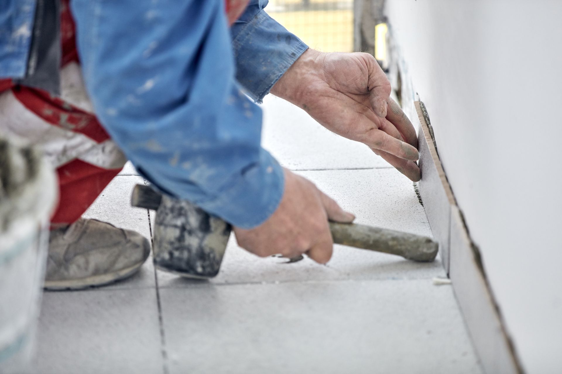 Person installing tile, using a hammer to tap a tile into place on a wall and floor.