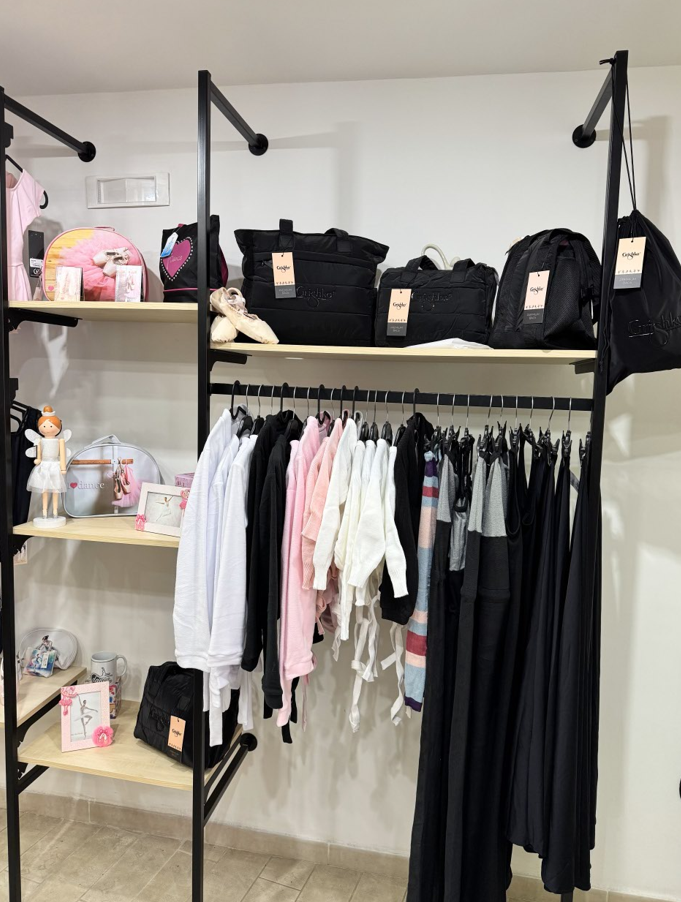 Esposizione di un negozio di abbigliamento con appendiabiti neri, borse e indumenti su scaffali di legno.