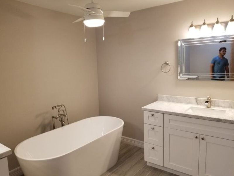 A bathroom with a bathtub , sink , mirror and ceiling fan.