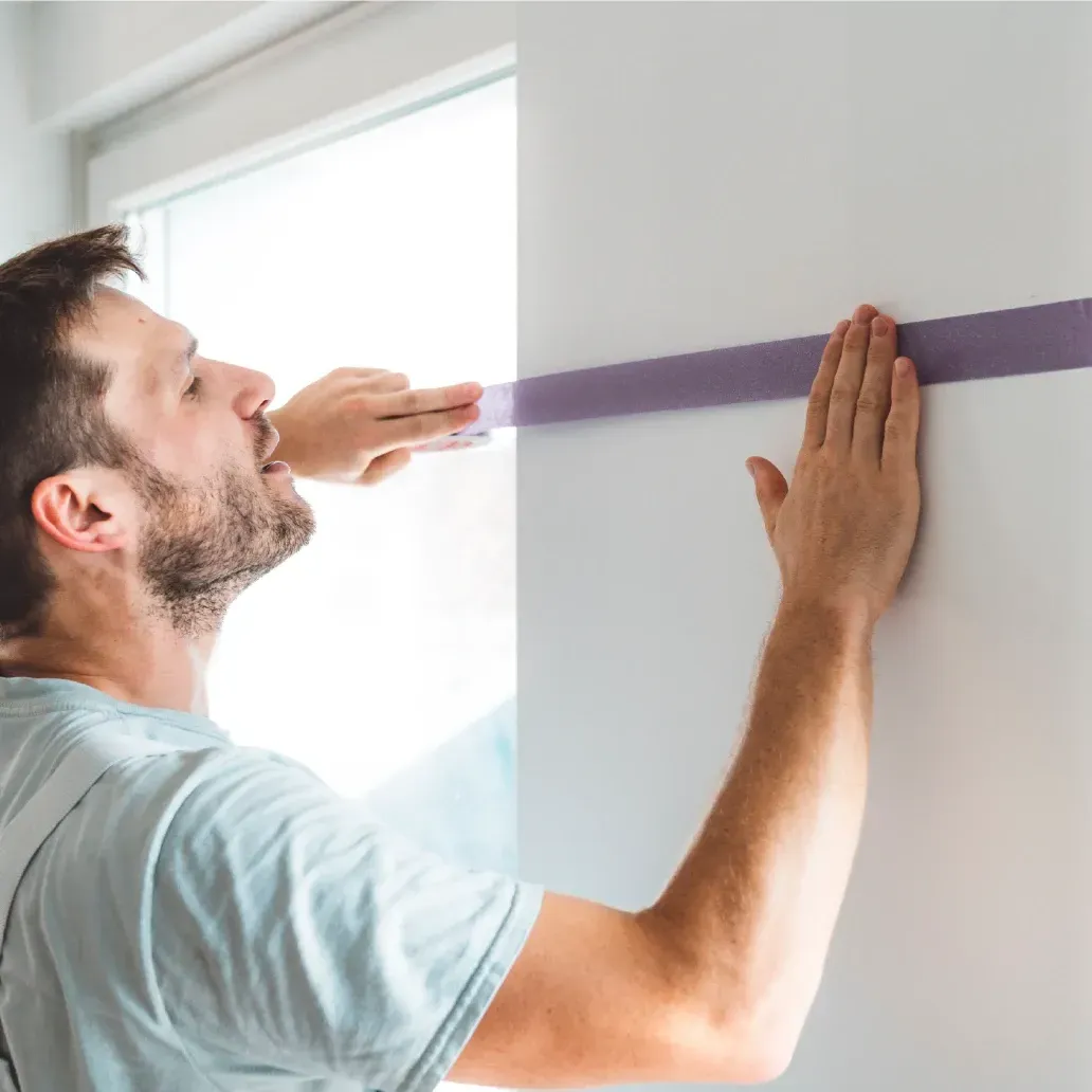 Ein Mann misst eine Wand mit lila Klebeband