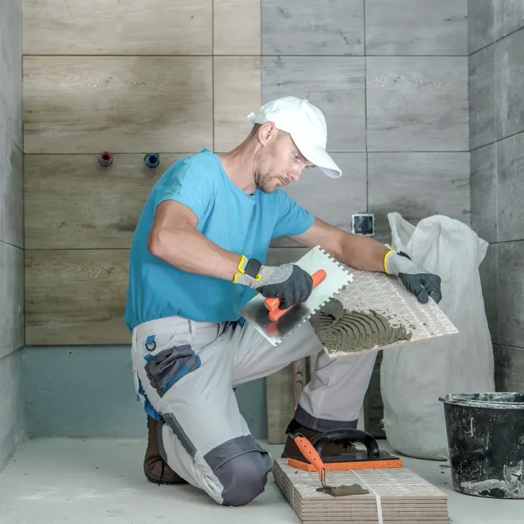 Badsanierung a man is kneeling down in a bathroom holding a piece of tile .