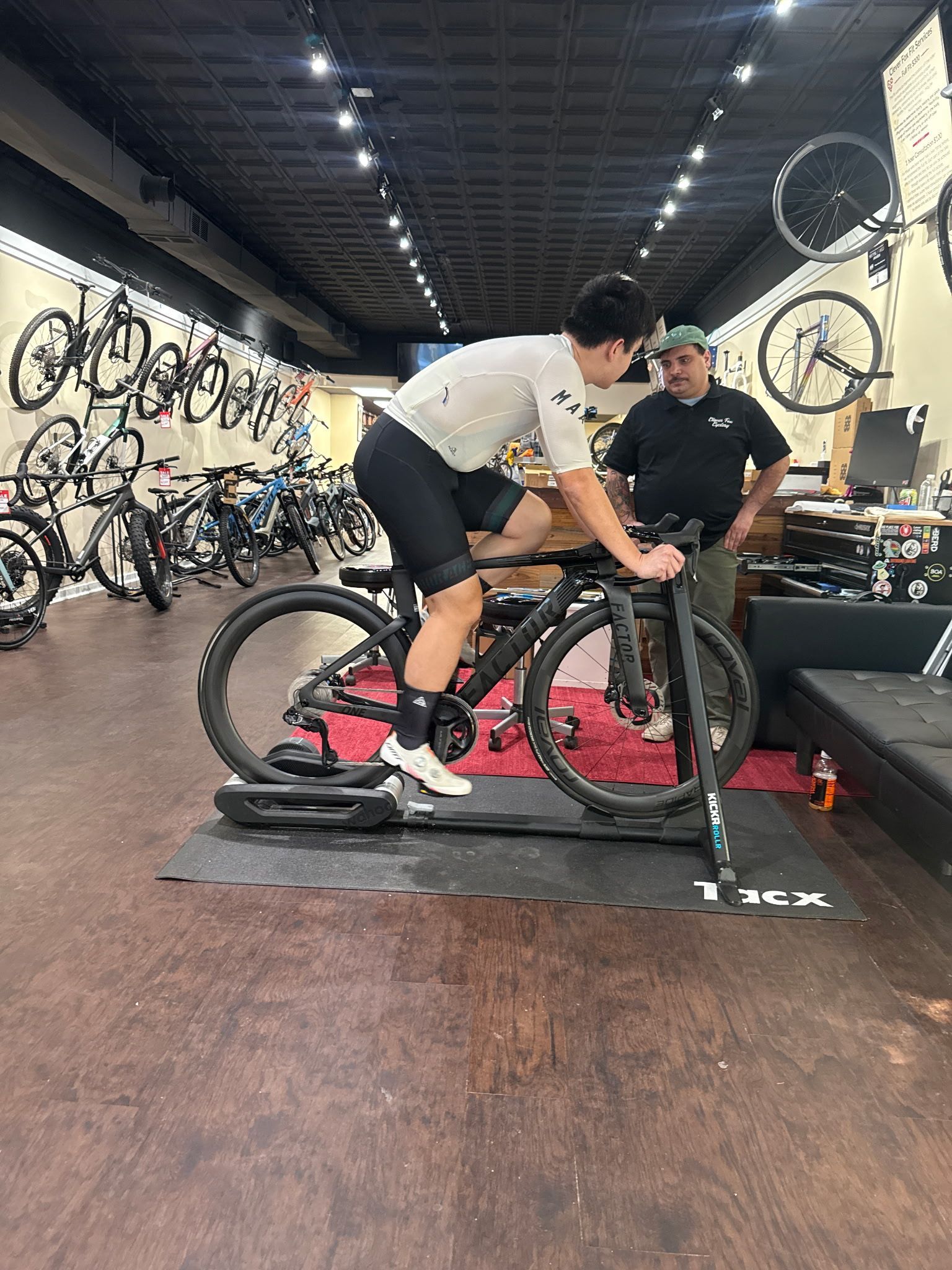 Cyclist on a pink bike getting a fitting in a bike shop while a mechanic adjusts the setup
