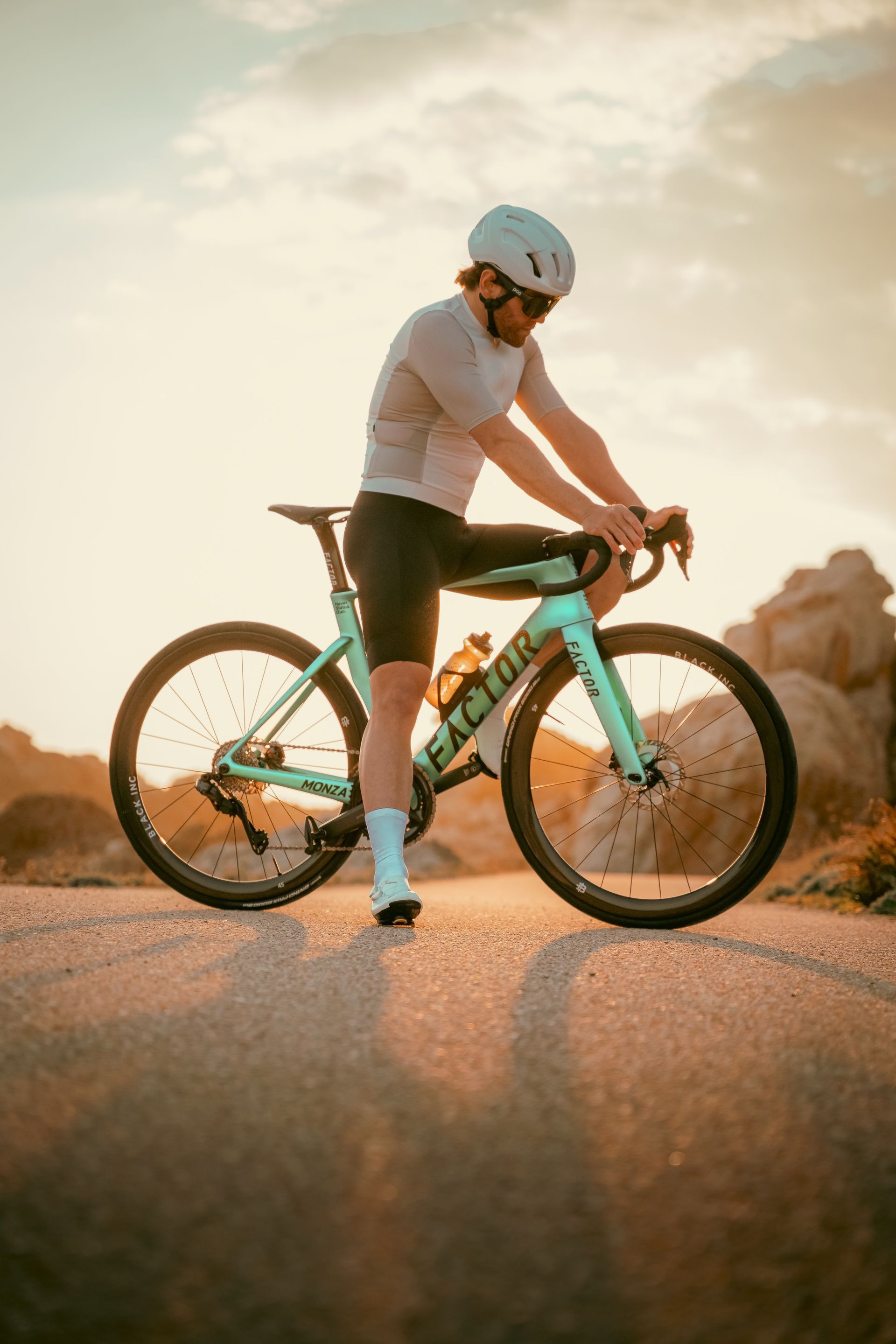 Cyclist on a turquoise bike riding on a sunlit dirt road at sunset