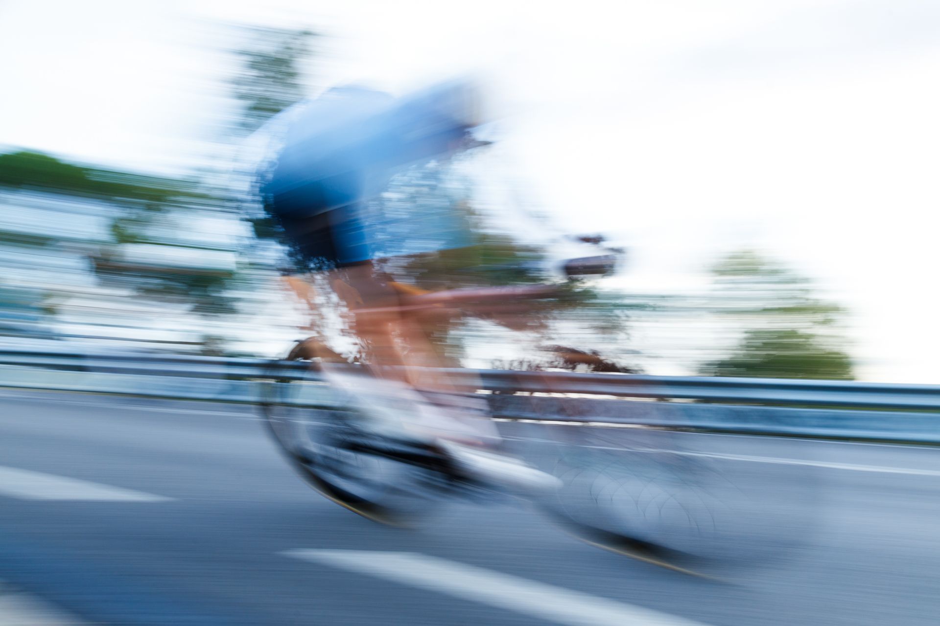 Blurred cyclist in blue racing along a road with motion streaks and a guardrail
