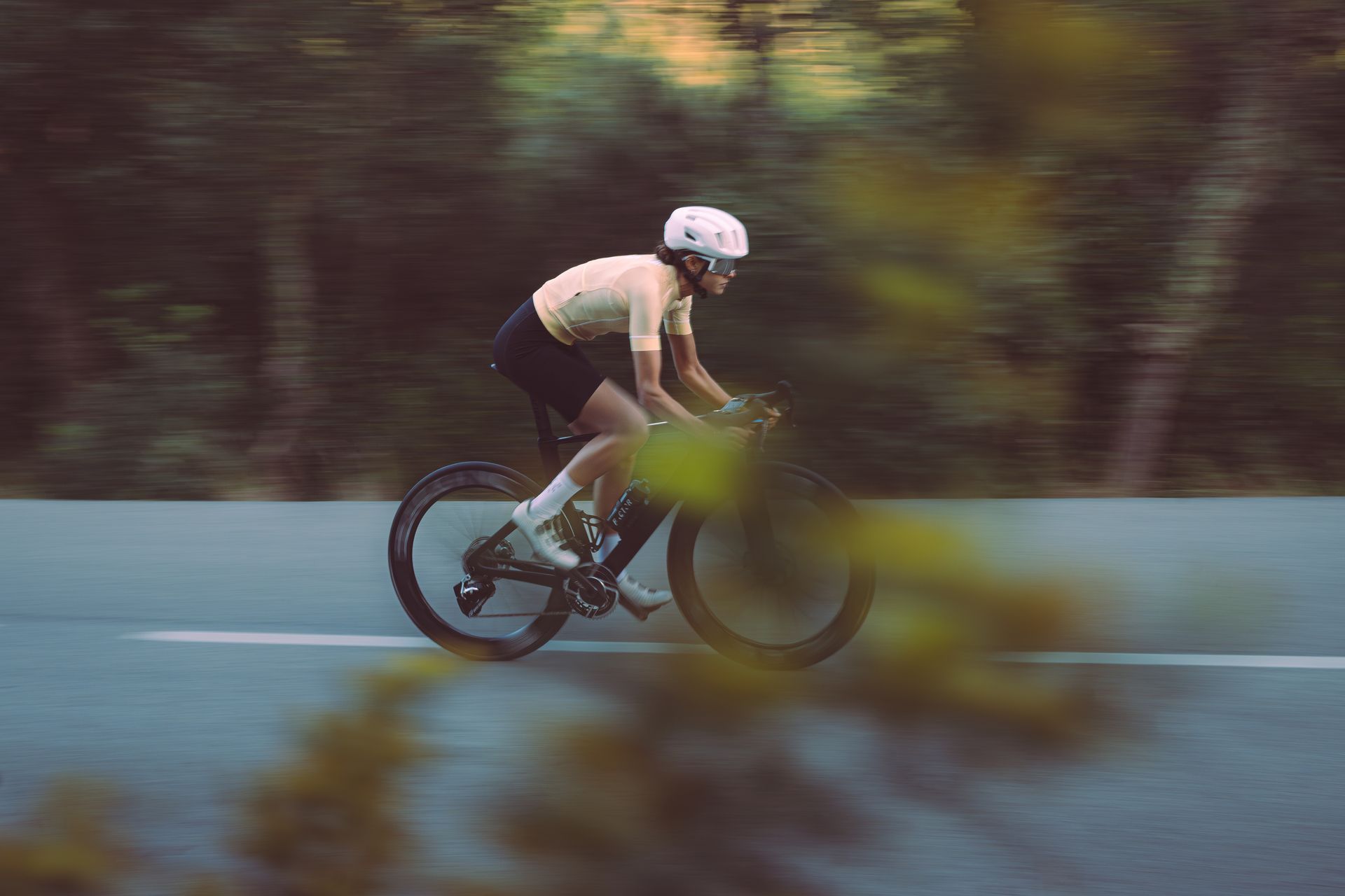 Cyclist in black gear riding fast on a blurred road, with motion blur and trees in the background