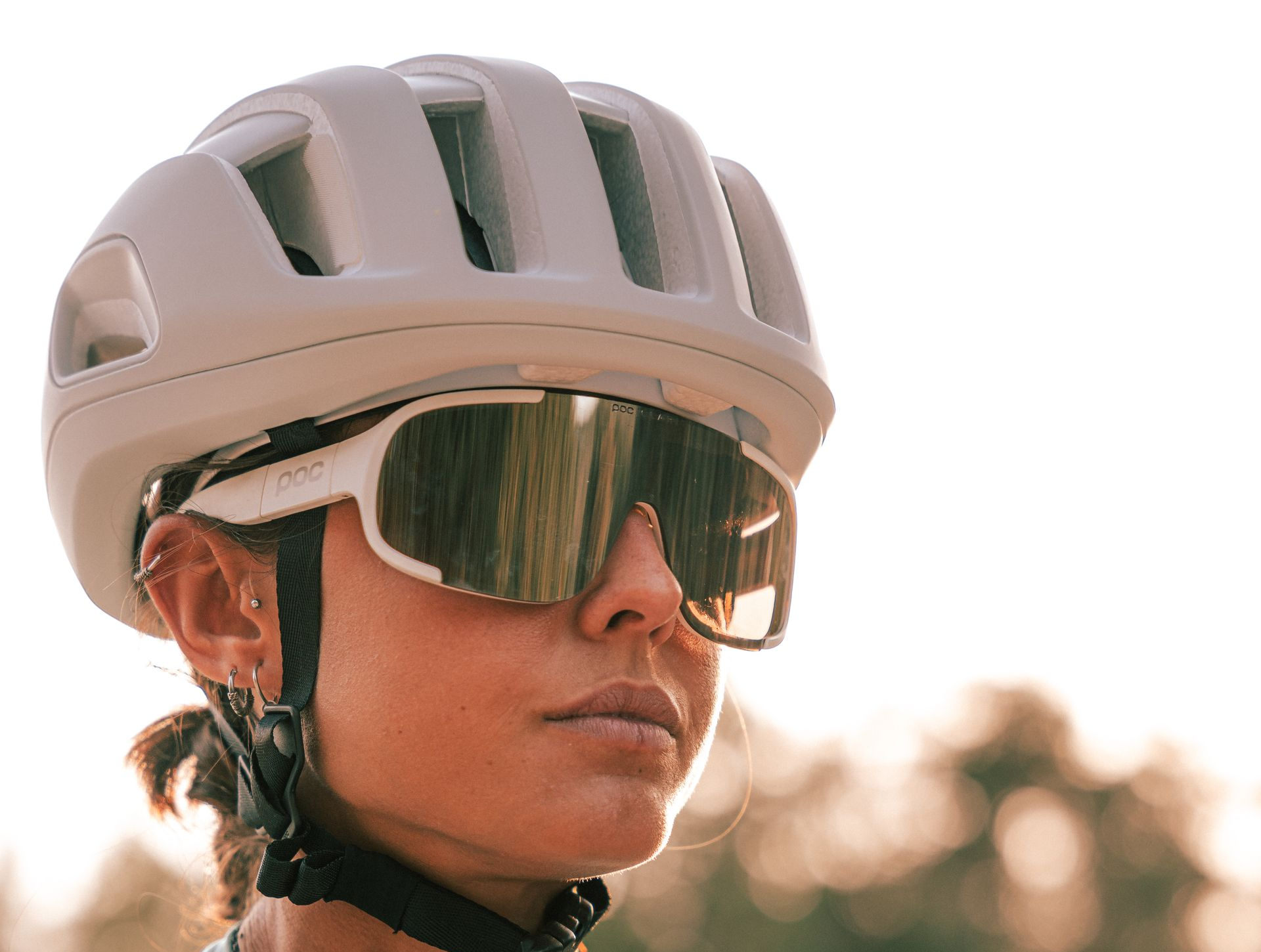Cyclist wearing a white helmet and mirrored sunglasses against a blurred outdoor background