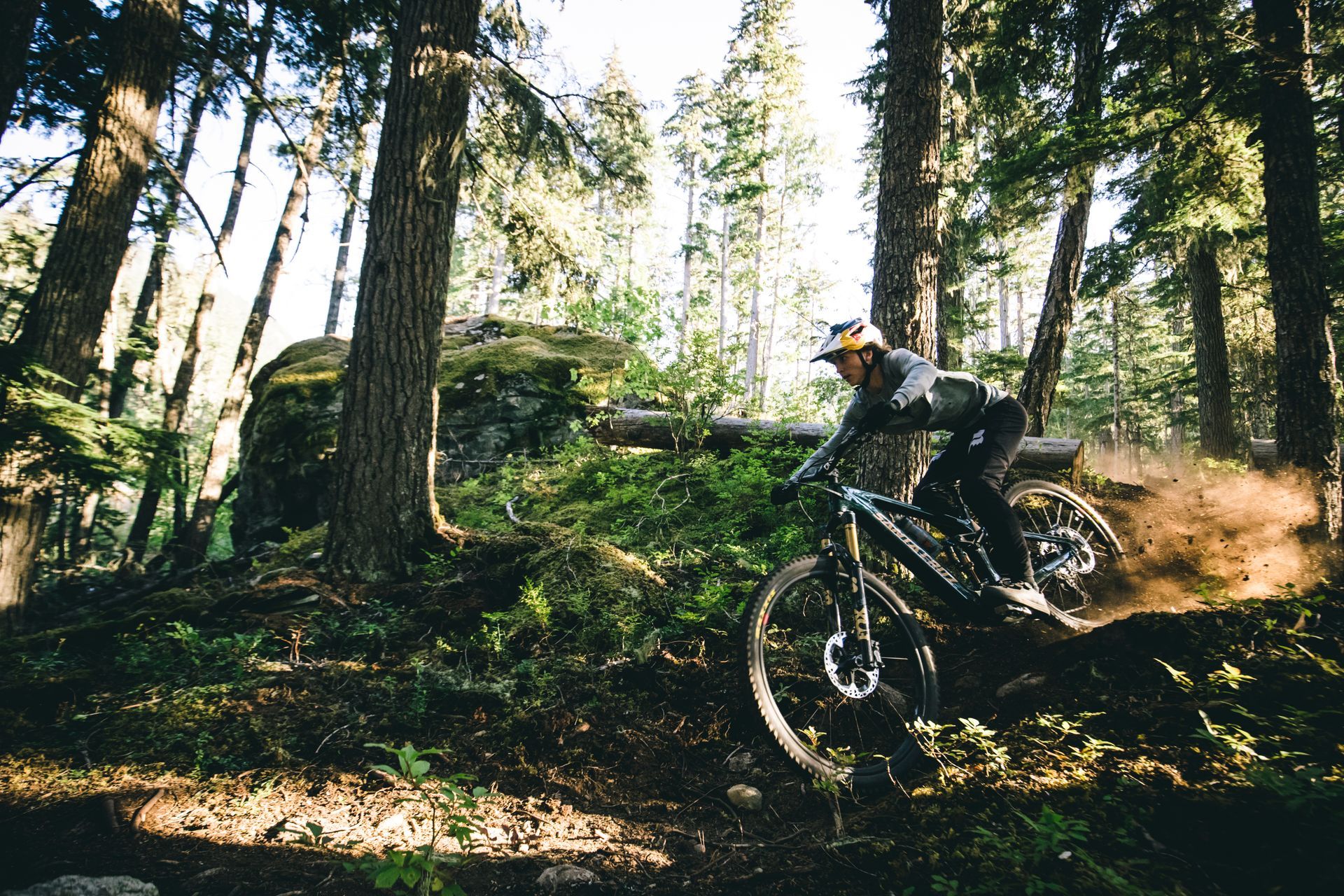 Woman riding electric mountain bike with fox factory suspension in a mountain bike trail wearing redbull team helmet
