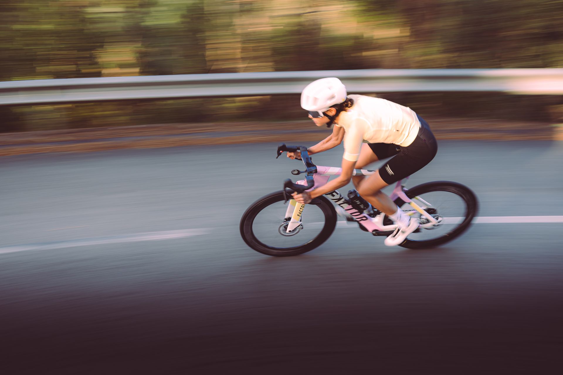 Cyclist in white helmet riding a black road bike on a wet road, motion blurred background