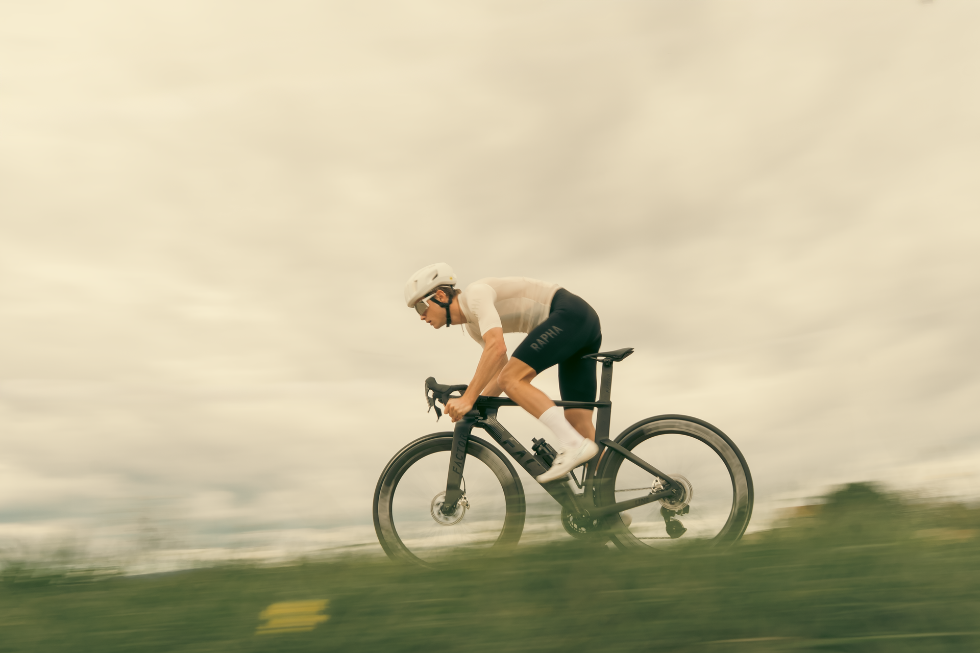 Cyclist riding fast on a road bike through a cloudy landscape