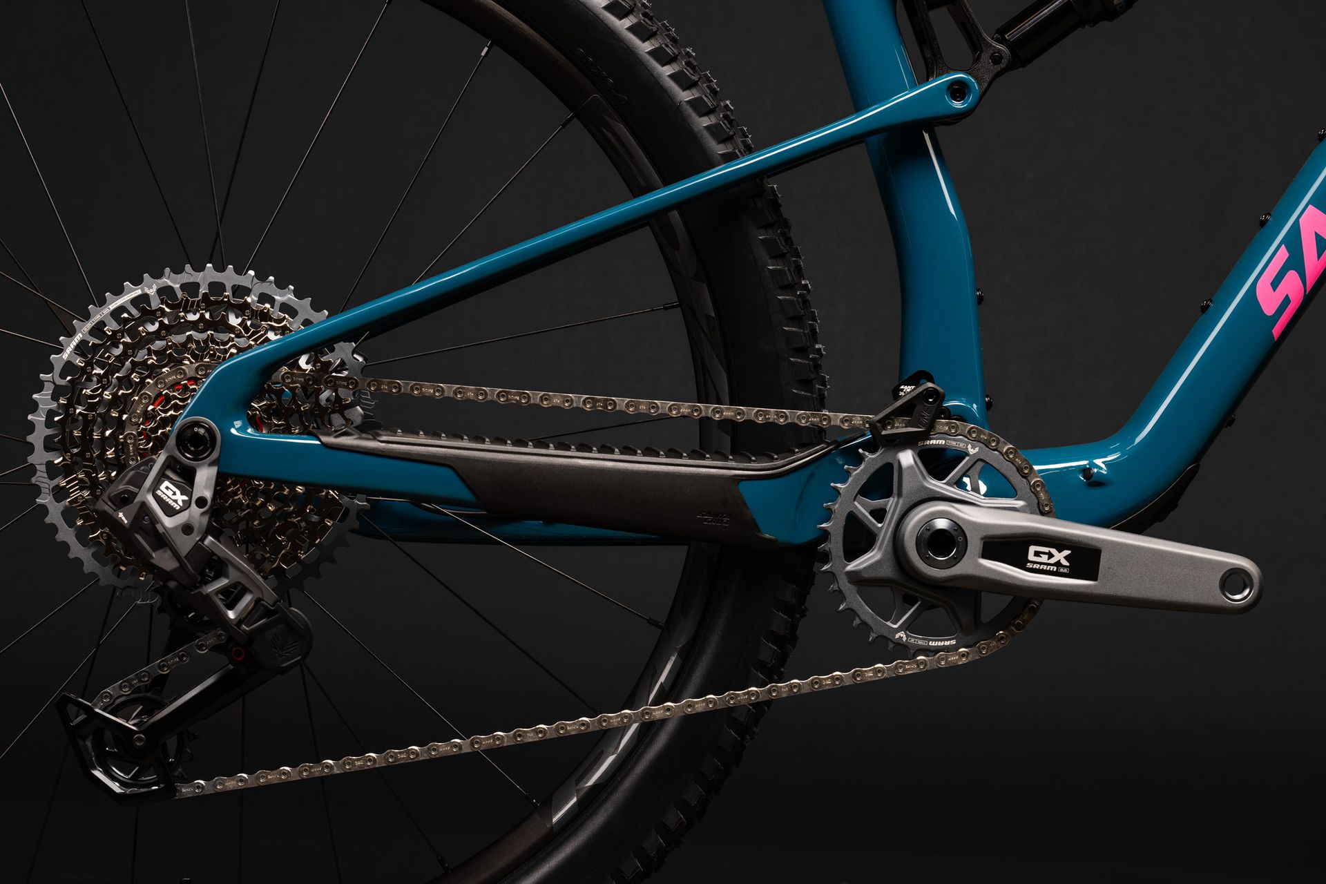 Cyclist’s legs and black bike with teal frame riding on a road near greenery