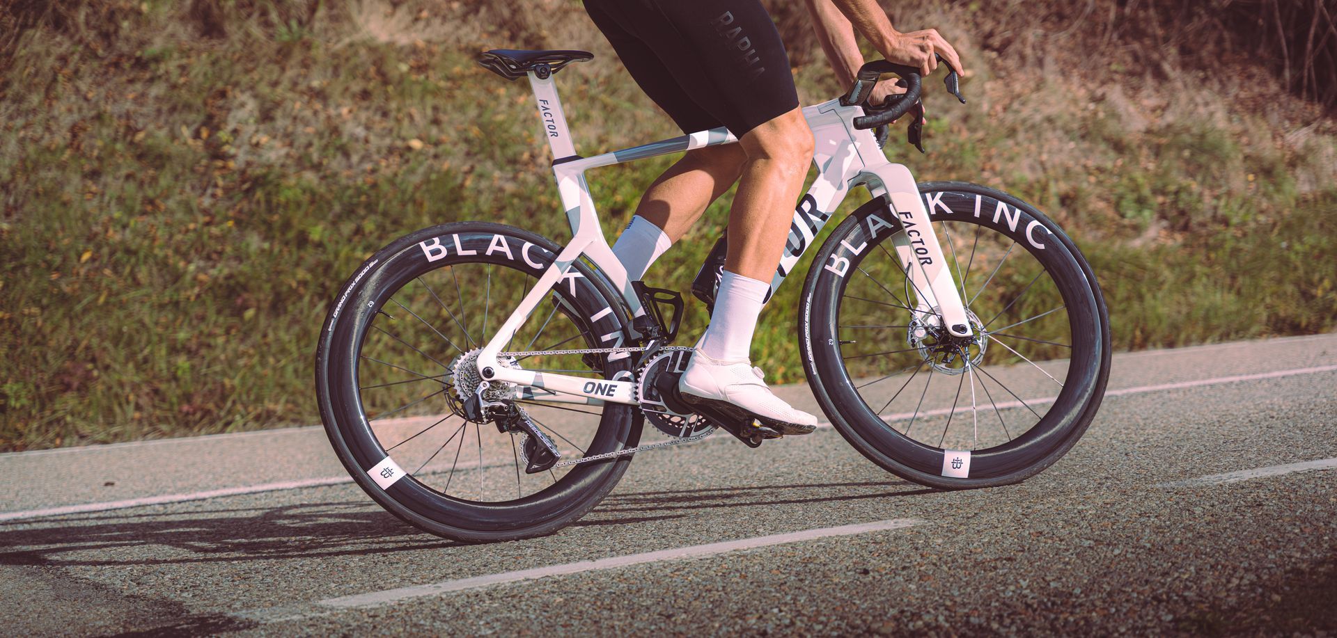 Cyclist riding a white bike on a roadside, wearing black shorts and white socks.