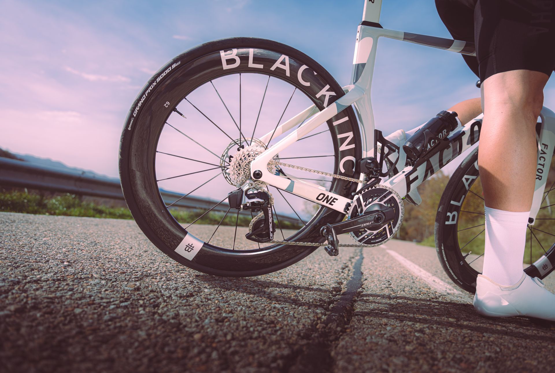 Low-angle view of a cyclist’s white bike and legs on a road at sunset