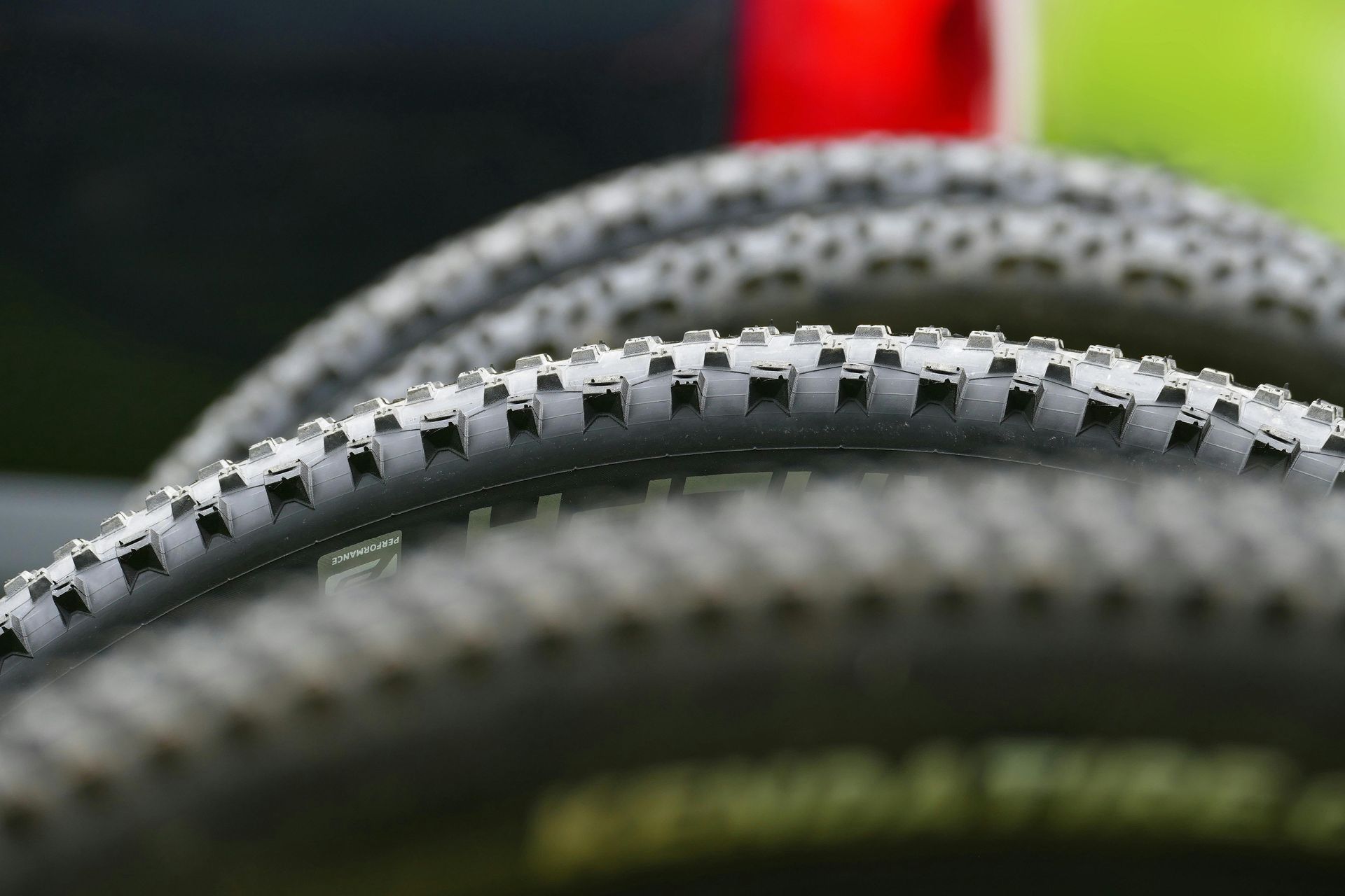 Close-up of two bicycle tires with black tread and a blurred red background
