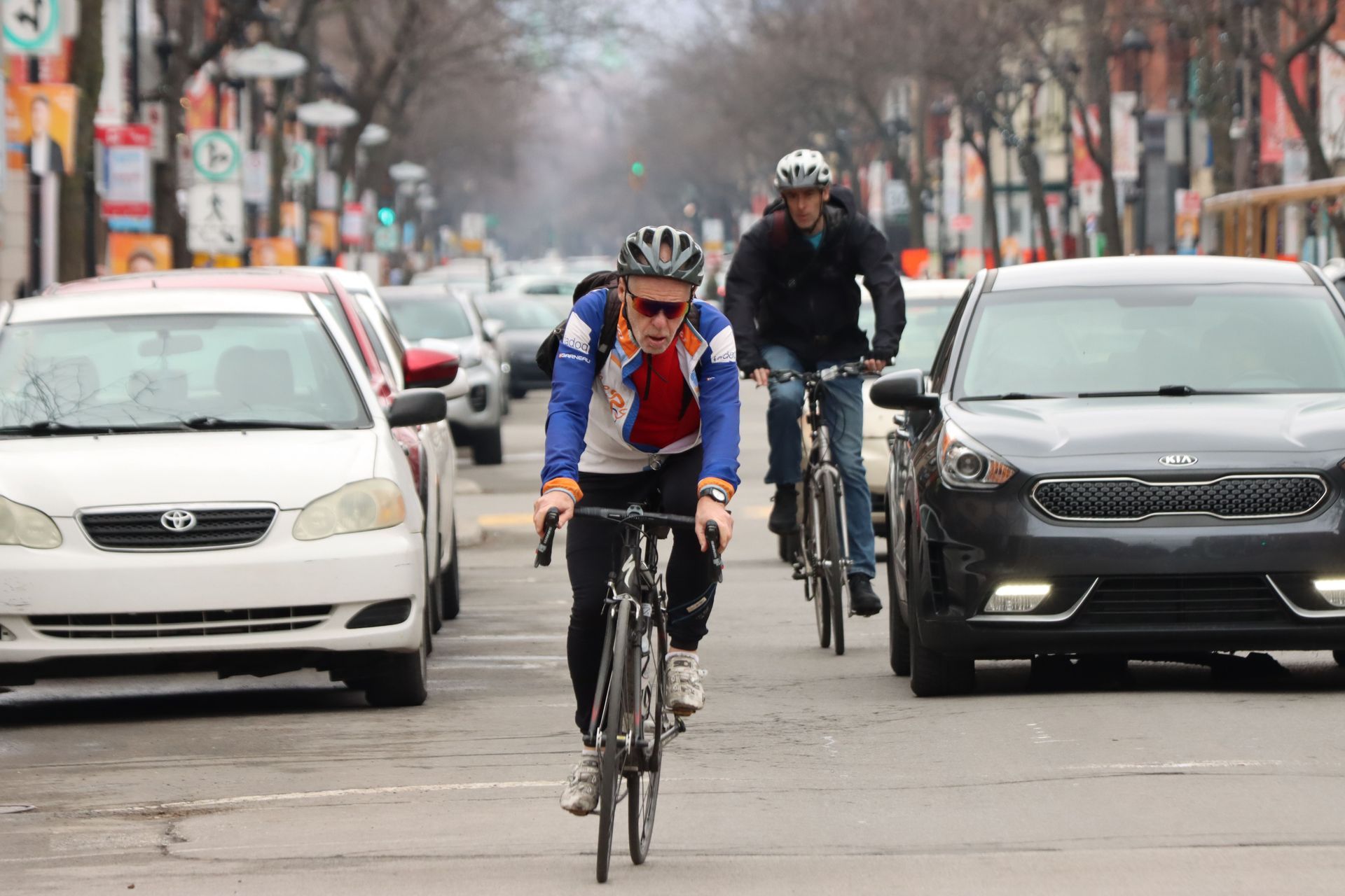 Cyclist in blue jacket riding down a city street with cars on both sides