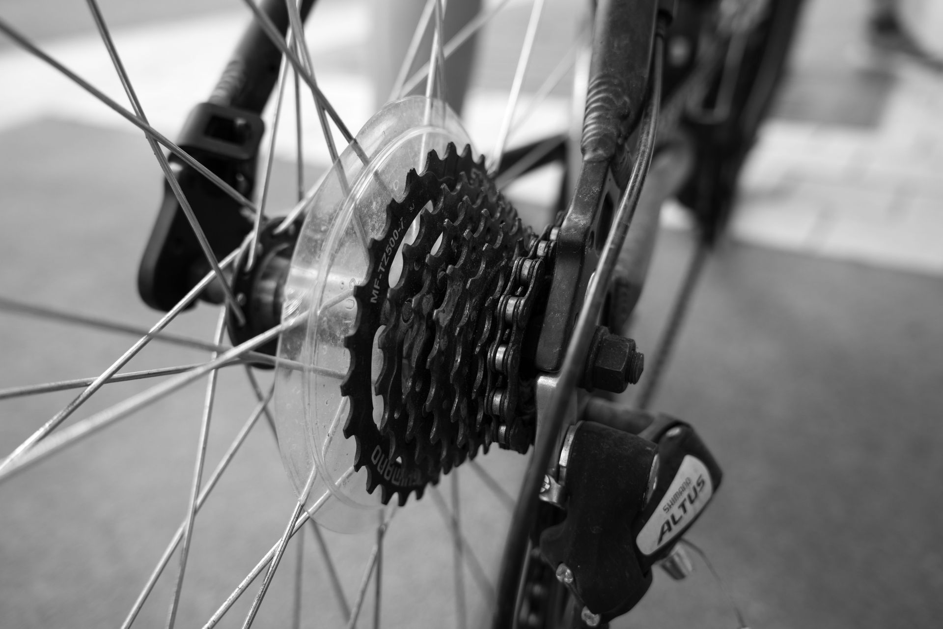 Close-up of a bicycle rear wheel, gear cassette, and derailleur in black and white.