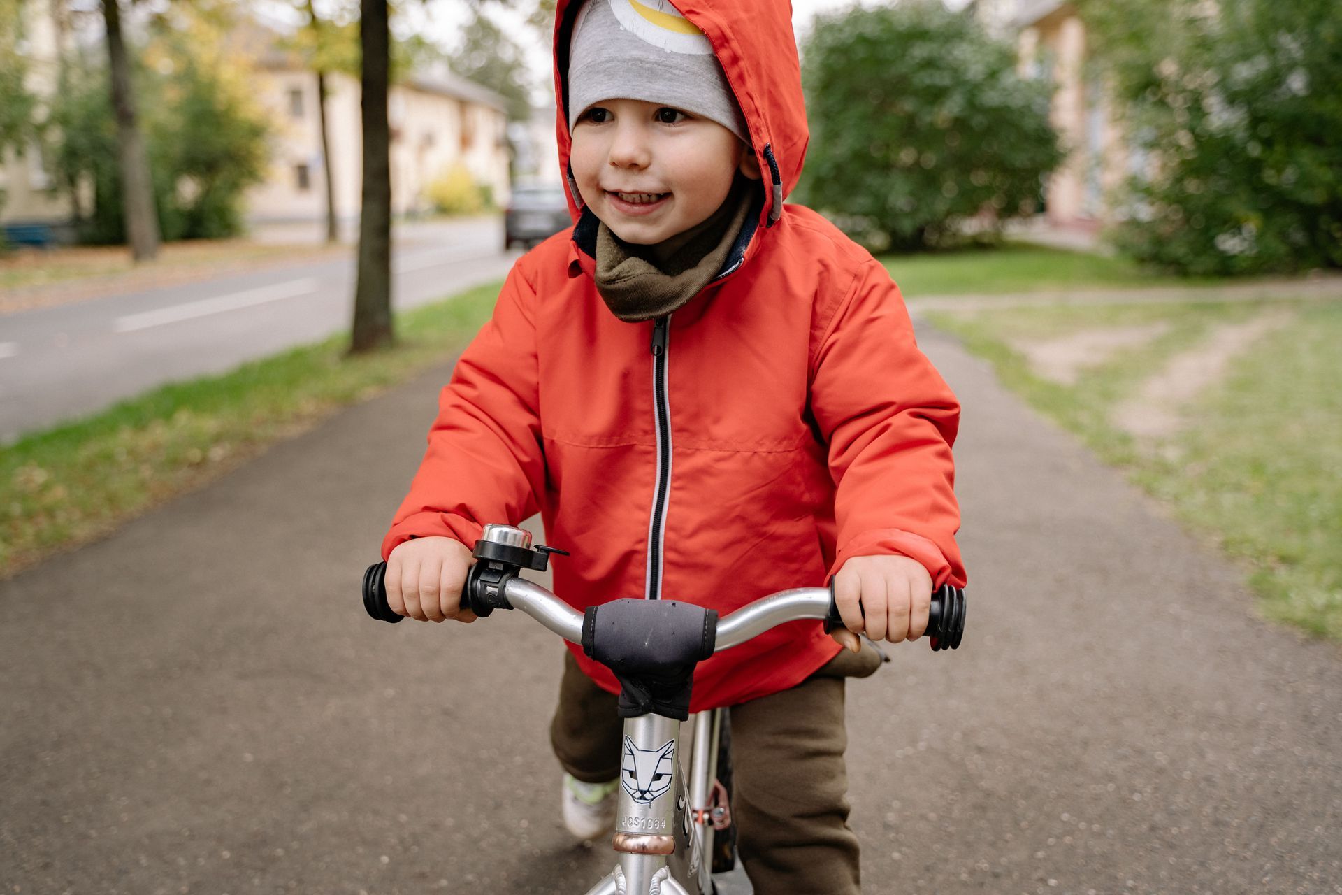 Child in a red jacket riding a strider bike on a paved path in a park