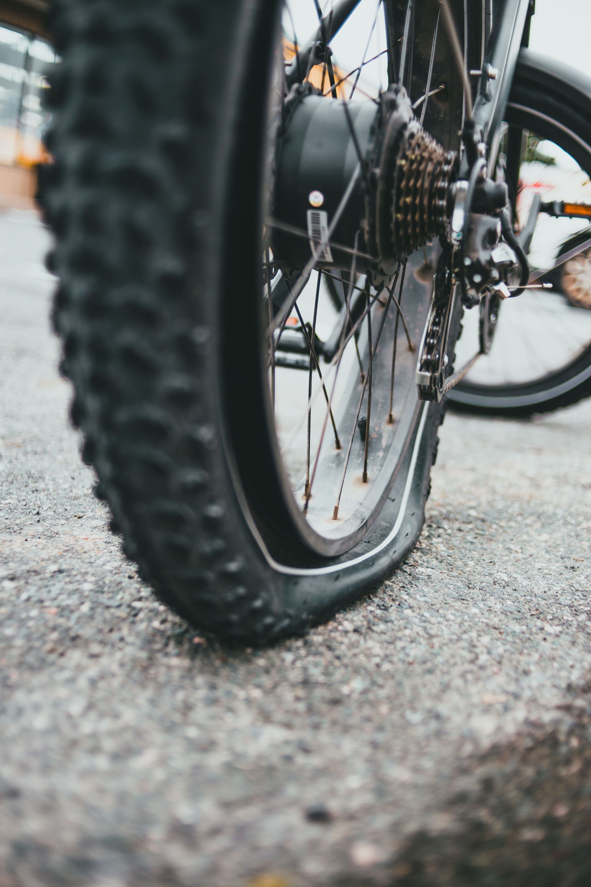 Close-up of a black bicycle tire on a paved road, with another bike blurred in the background