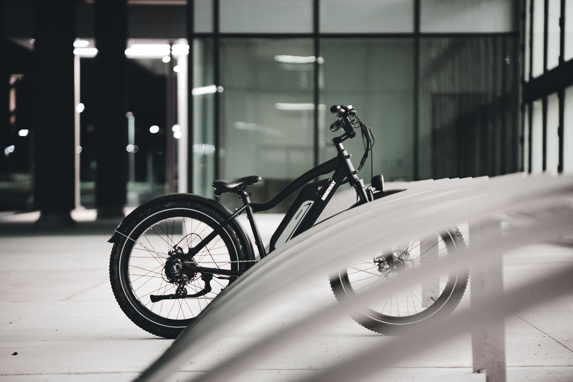 Black bicycle parked indoors beside a blurred car in a modern glass building lobby