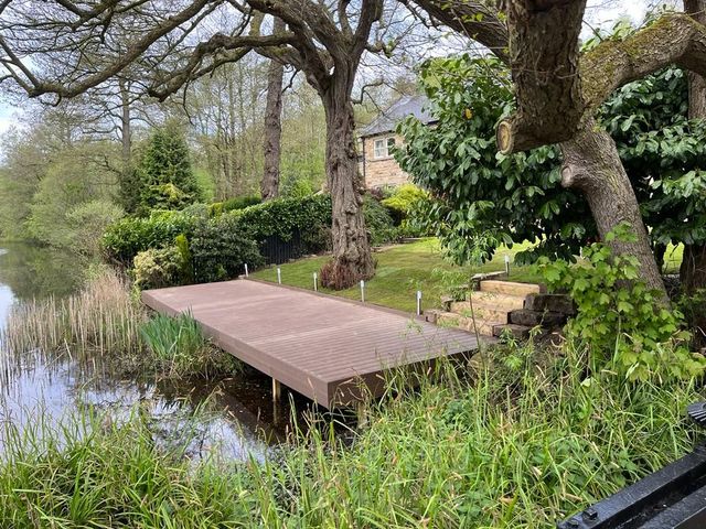 Brown composite decking jetty built out over a lake with inset deck lights and stone steps up to the garden