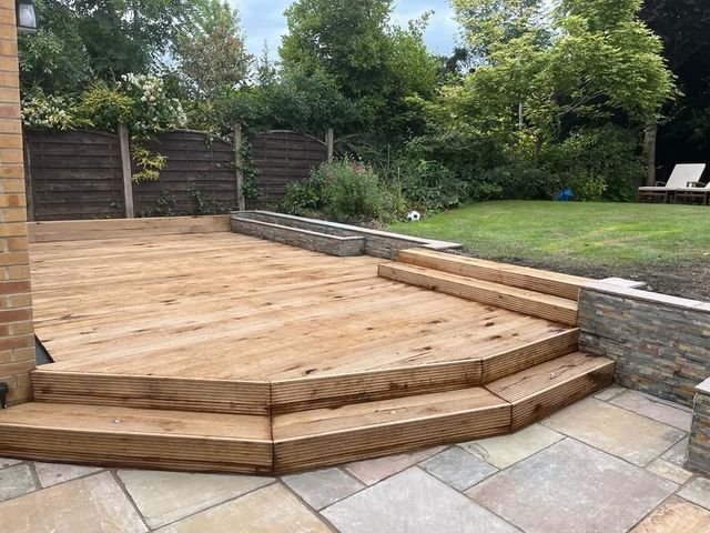Timber decking with angled corner steps down to a stone flag patio and raised planting beds in Bradway, Sheffield