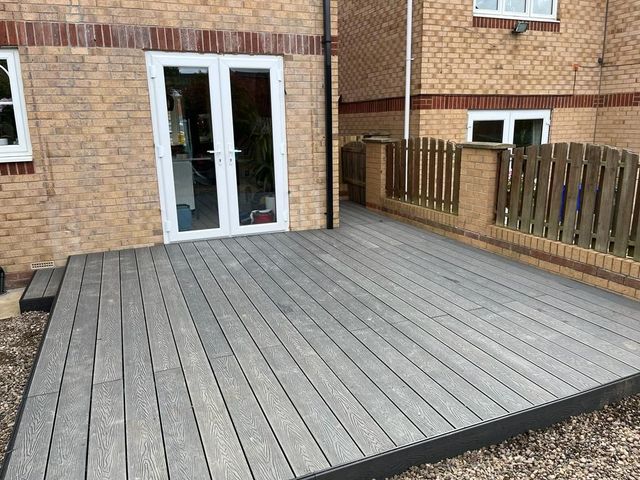 Ground level grey composite decking laid outside French doors at a brick house in Chapeltown, Sheffield