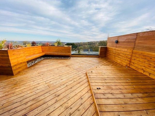 Roof top timber decking with a corner bench seat, slatted screen and glass balustrade looking out over Sheffield