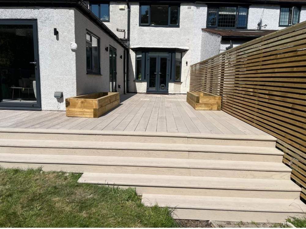Cream composite decking with wide steps down to a lawn, timber sleeper planters and a slatted privacy screen in Dore, Sheffield