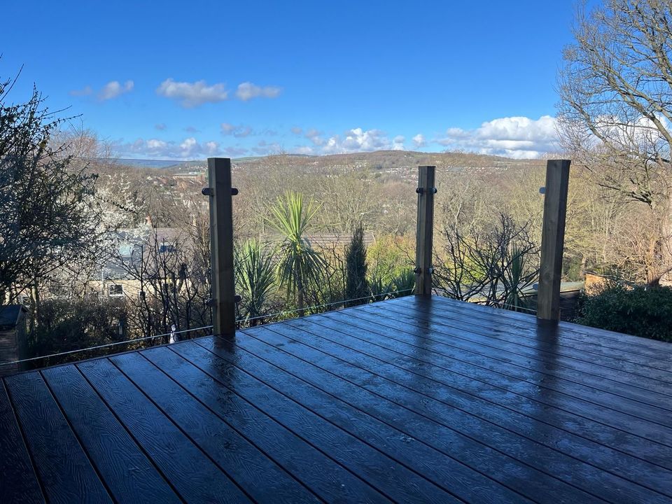 Raised dark composite deck with a glass balustrade looking out over a wooded valley