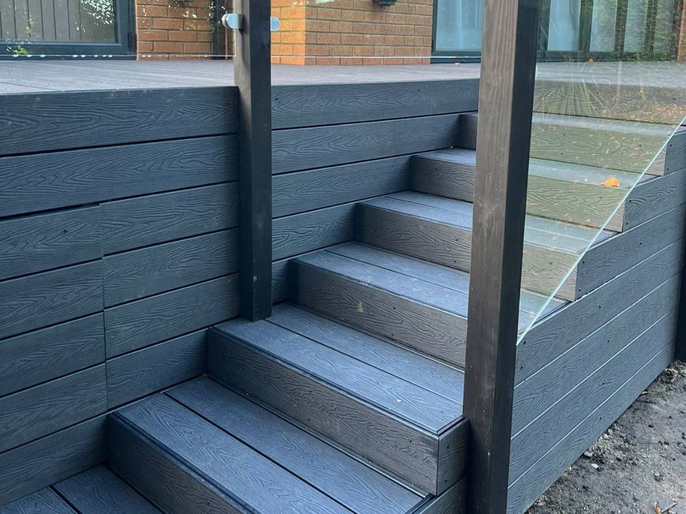 Steps clad in black composite boards rising beside a frameless glass balustrade