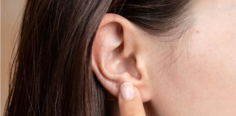 A close up of a woman pointing to her ear.