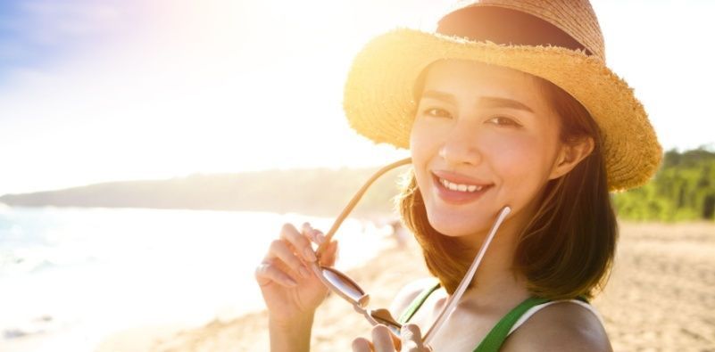 A woman at the beach, holding sunglasses in her hands