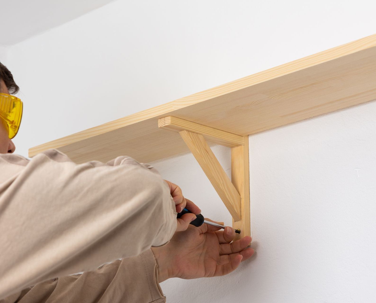 A man is working on a wooden shelf with a screwdriver
