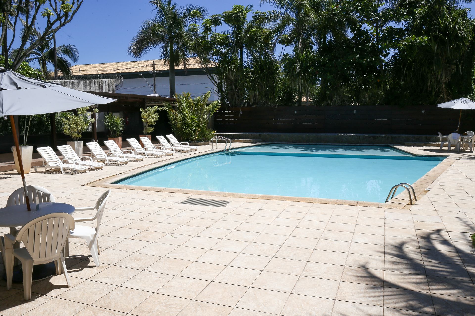 Área da piscina com espreguiçadeiras, guarda-sóis e uma piscina de água azul cristalina.