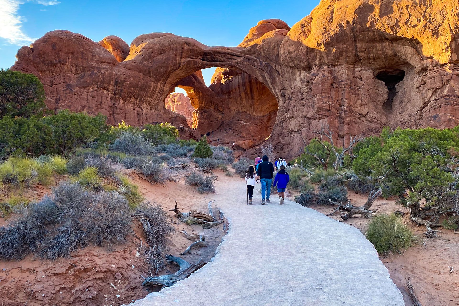 A group of people are walking towards Double Arch in Arches National Park.