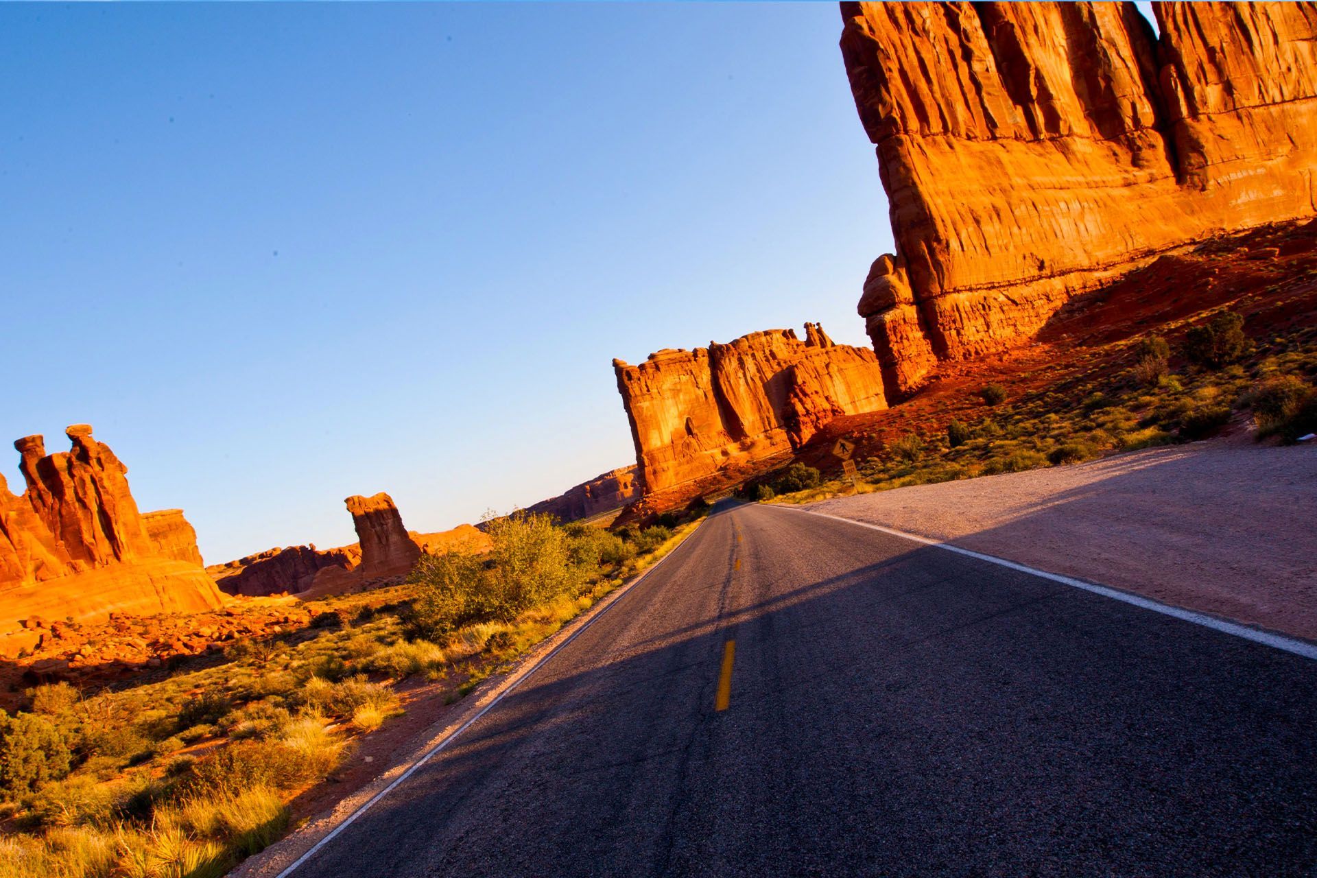Desert road through red rock formations under a clear blue sky.