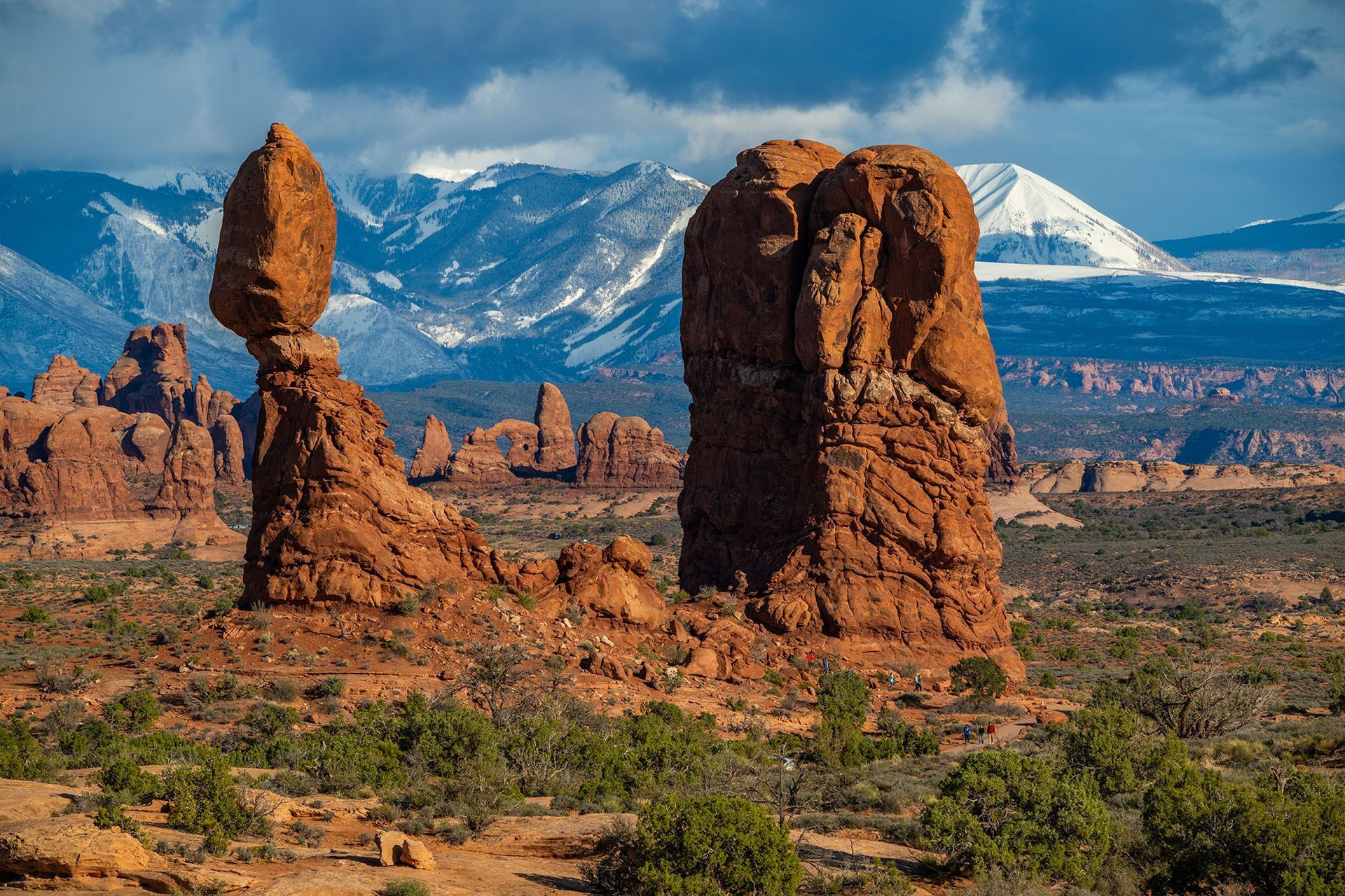 Balanced Rock in Arches National Park, Utah, with red rock formations and snow-capped mountains.