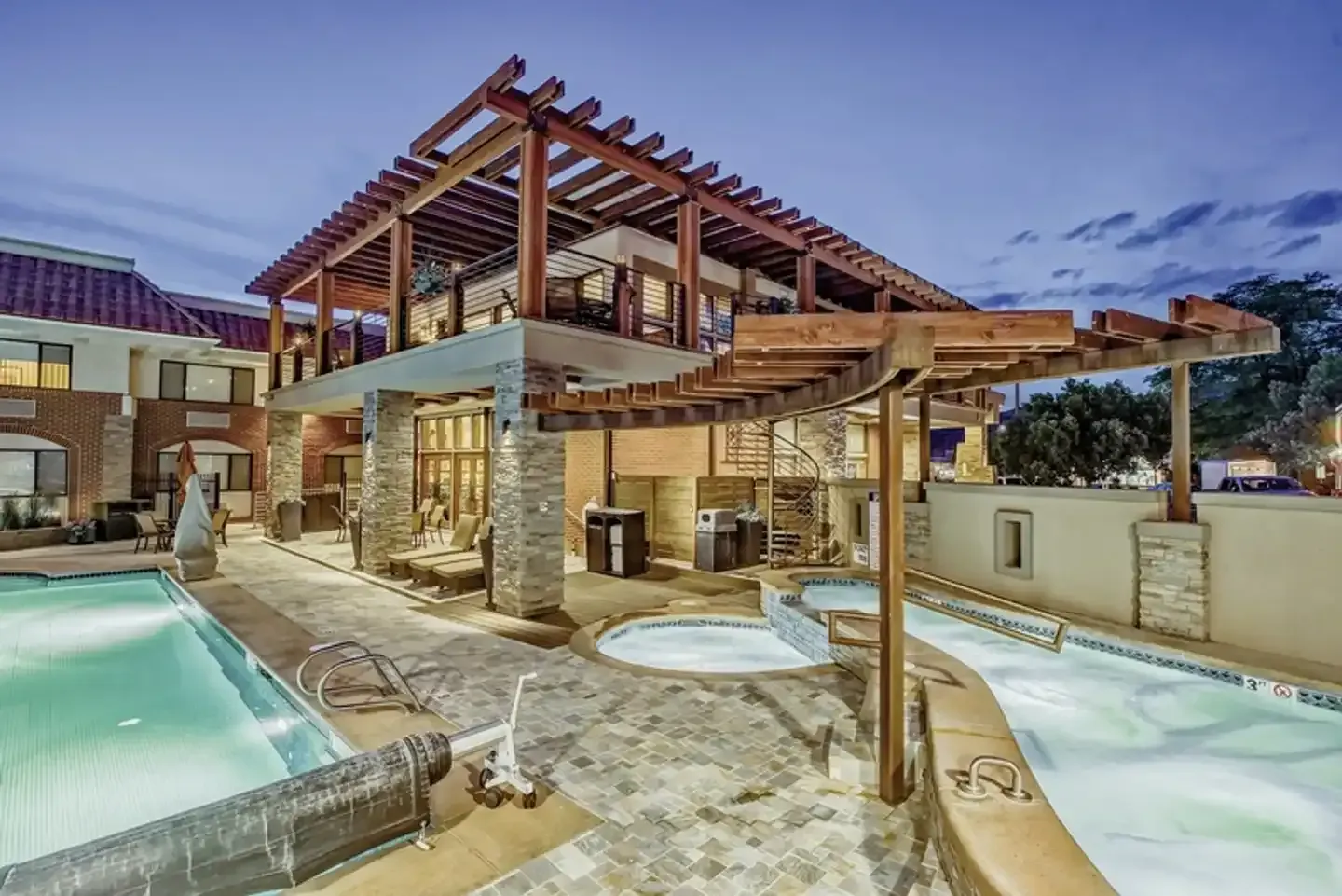 Hotel outdoor pool and spa area with a wood pergola at dusk.