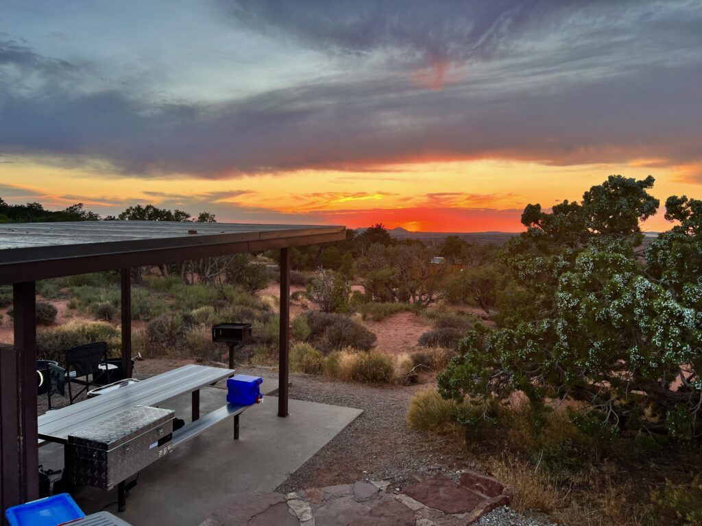 Sunset over a desert landscape; a covered picnic area is in the foreground.