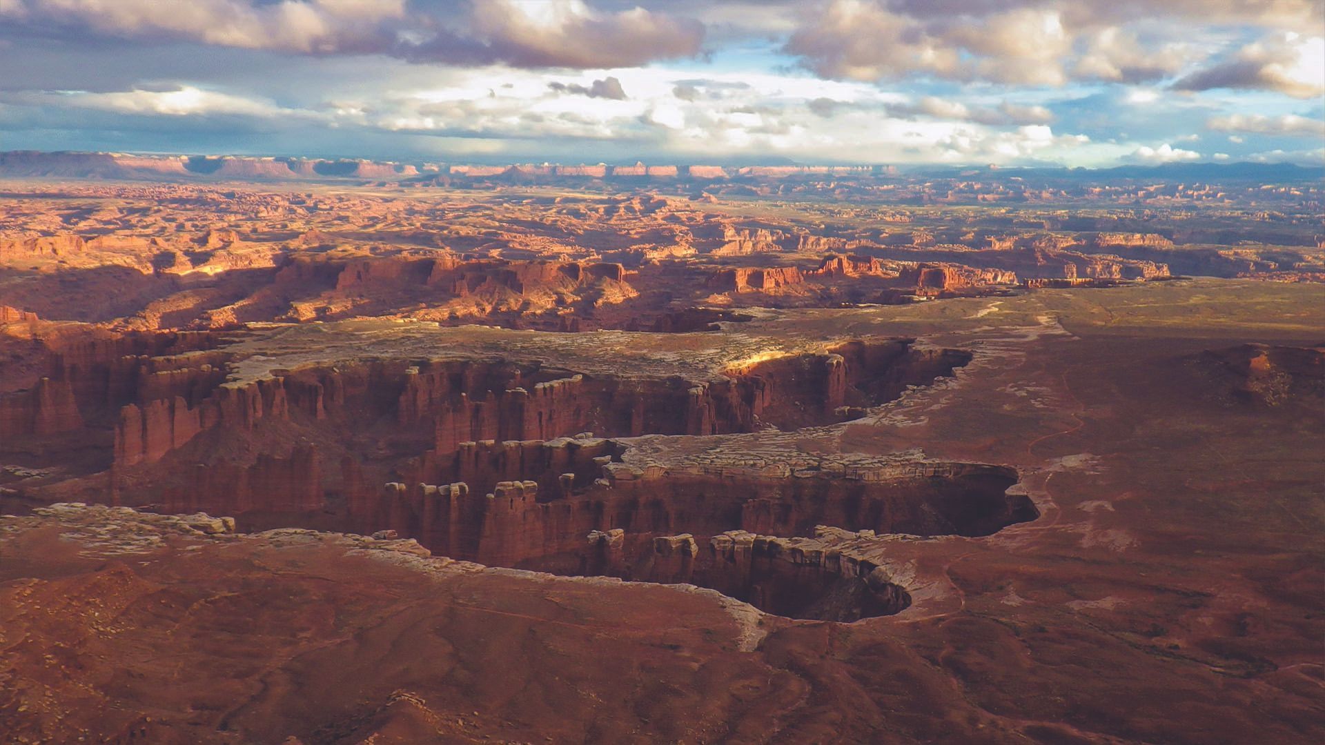Canyonlands National Park landscape with red rock formations and sunlit cliffs under cloudy sky.
