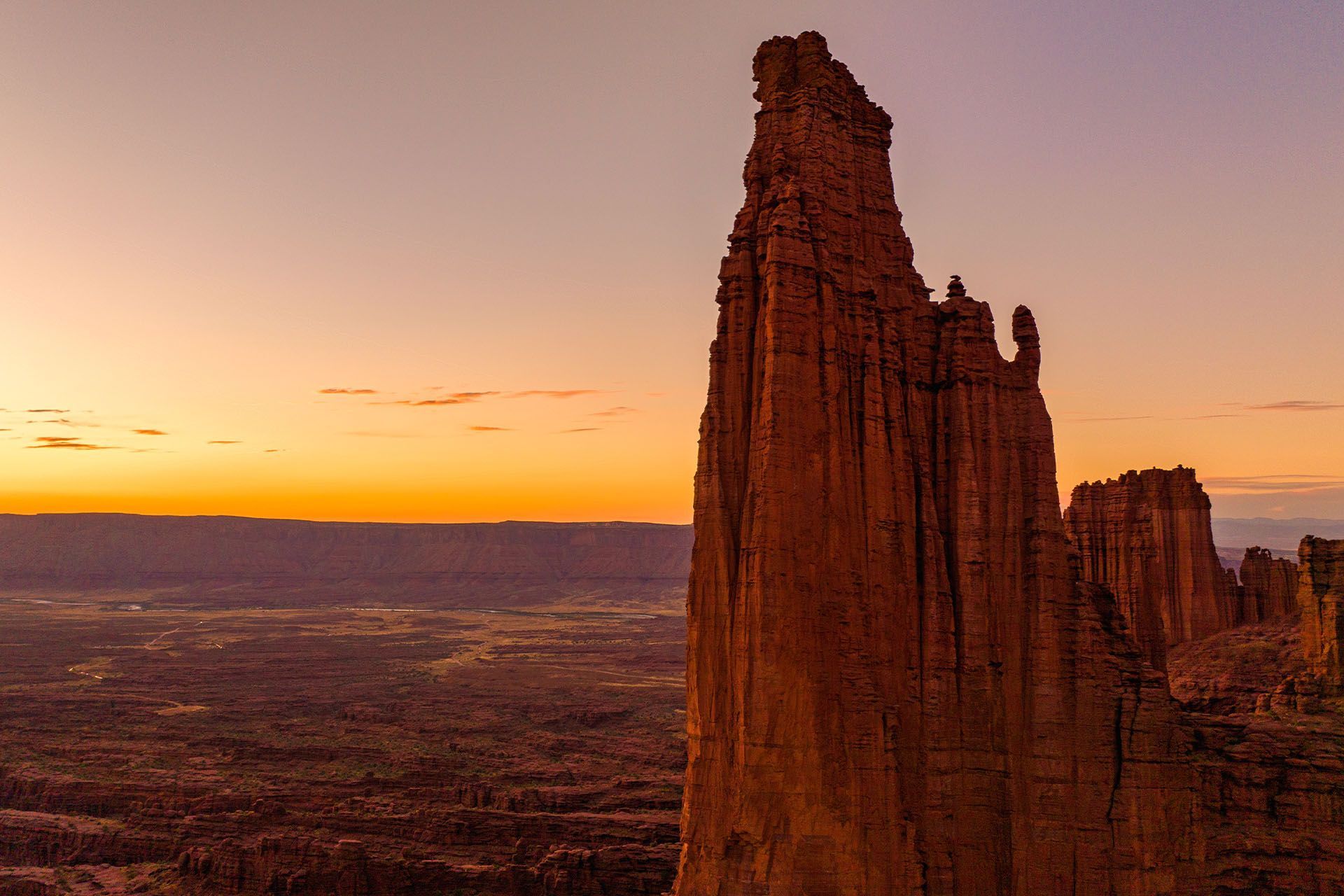 Tall red rock spire against a colorful sunset in a desert landscape.