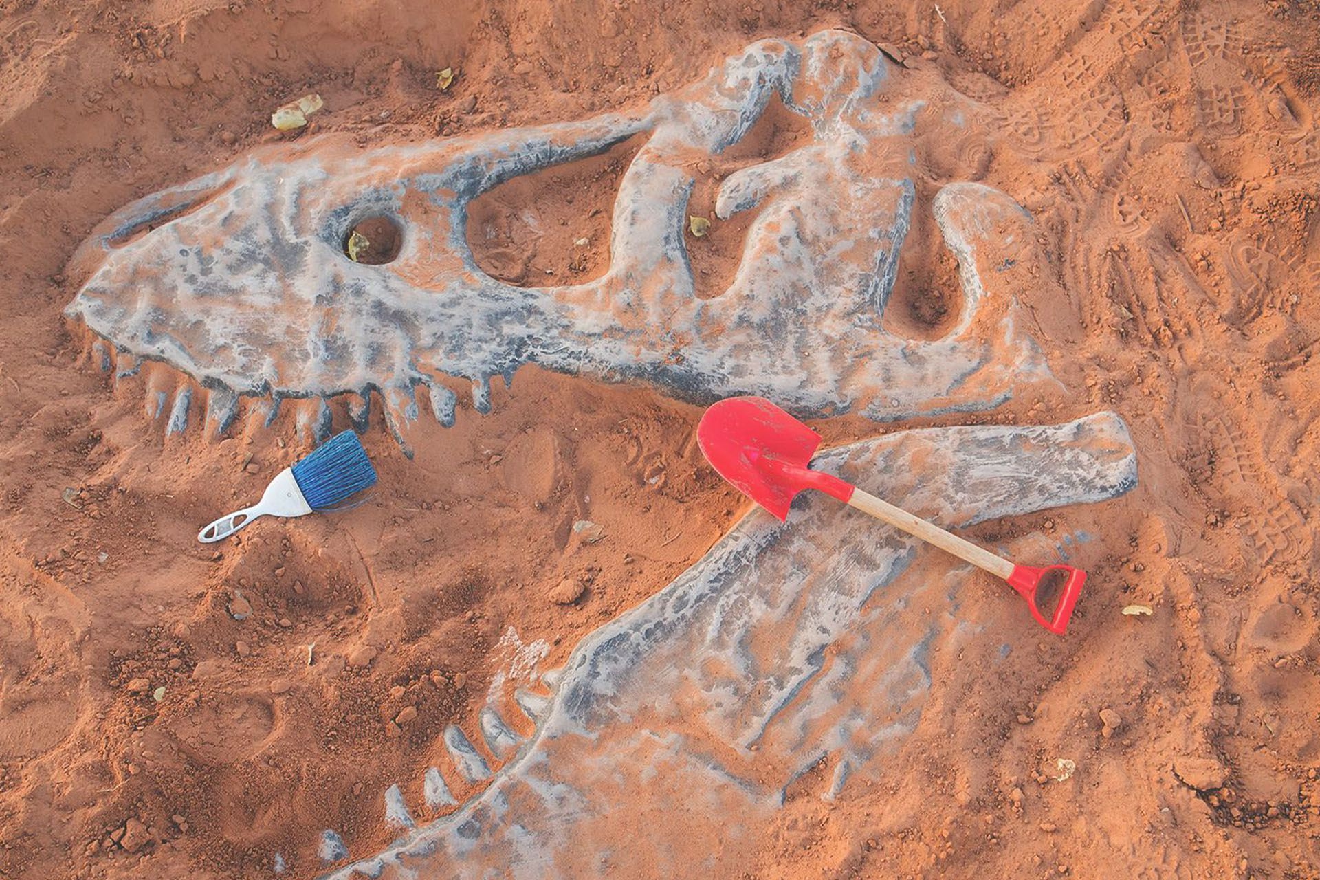 Dinosaur bones appear in the sand with children's digging tools scattered nearby.