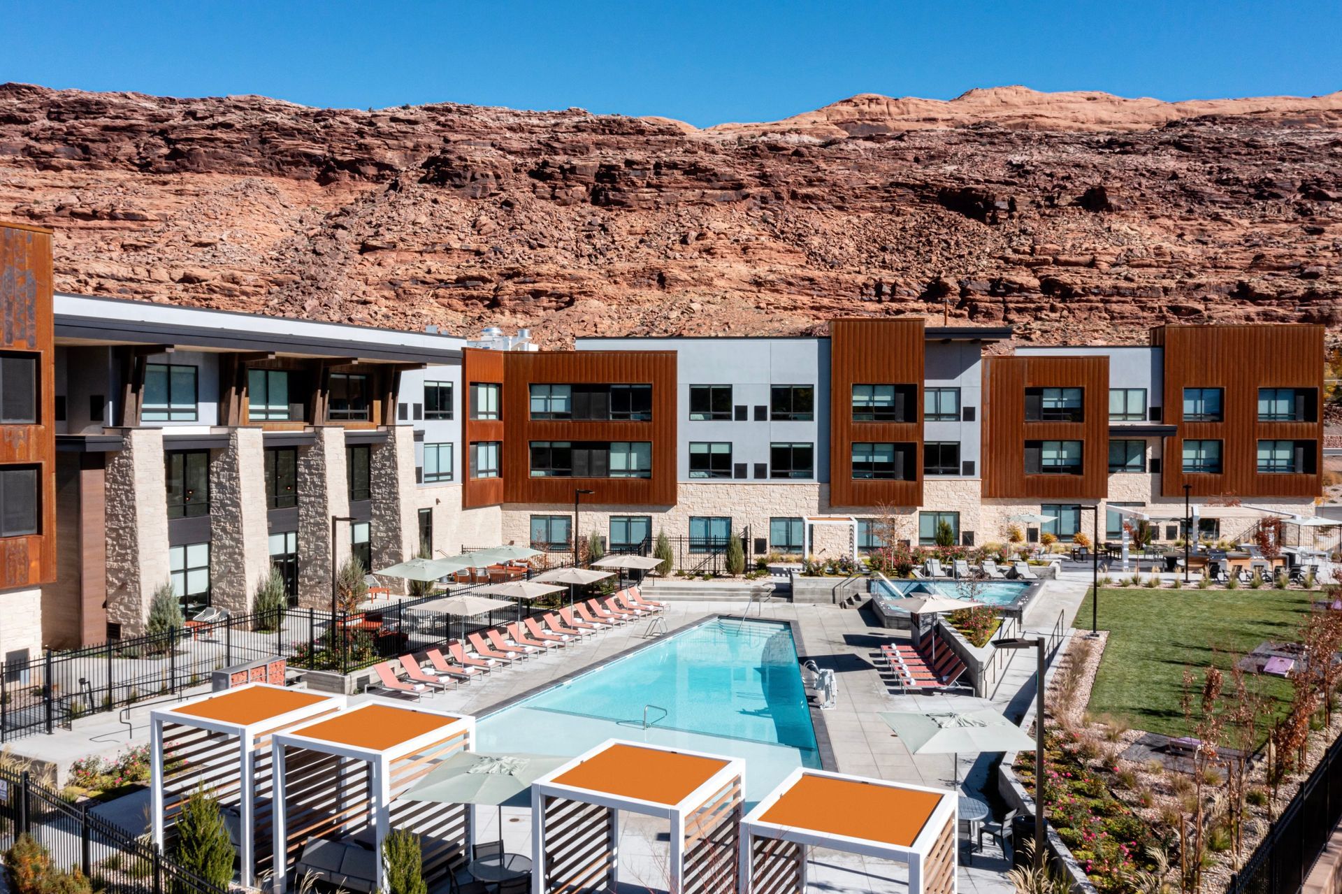 Apartment complex with pool, outdoor seating, and red rock backdrop.
