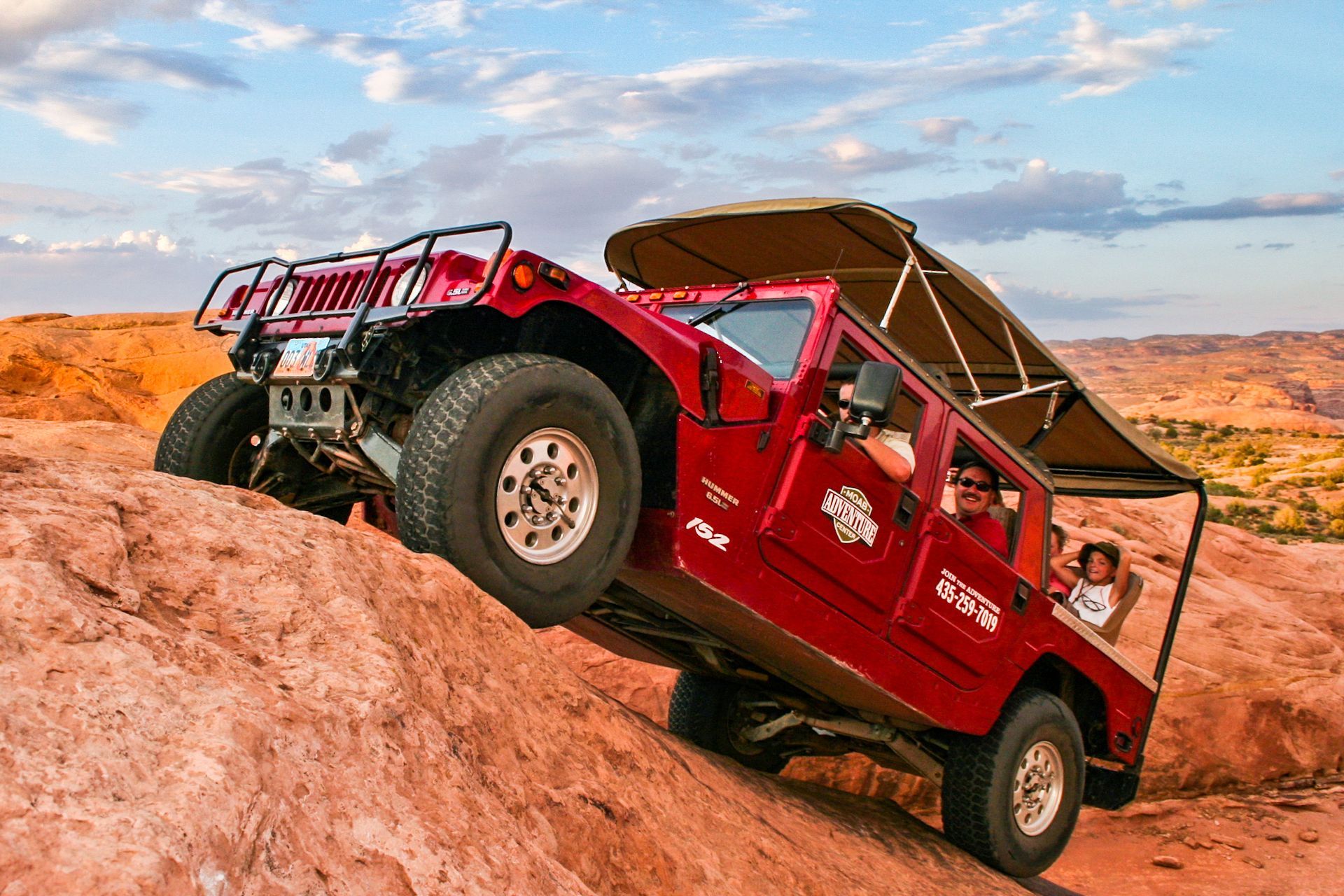 Red Hummer climbing a red rock hillside; passengers inside.
